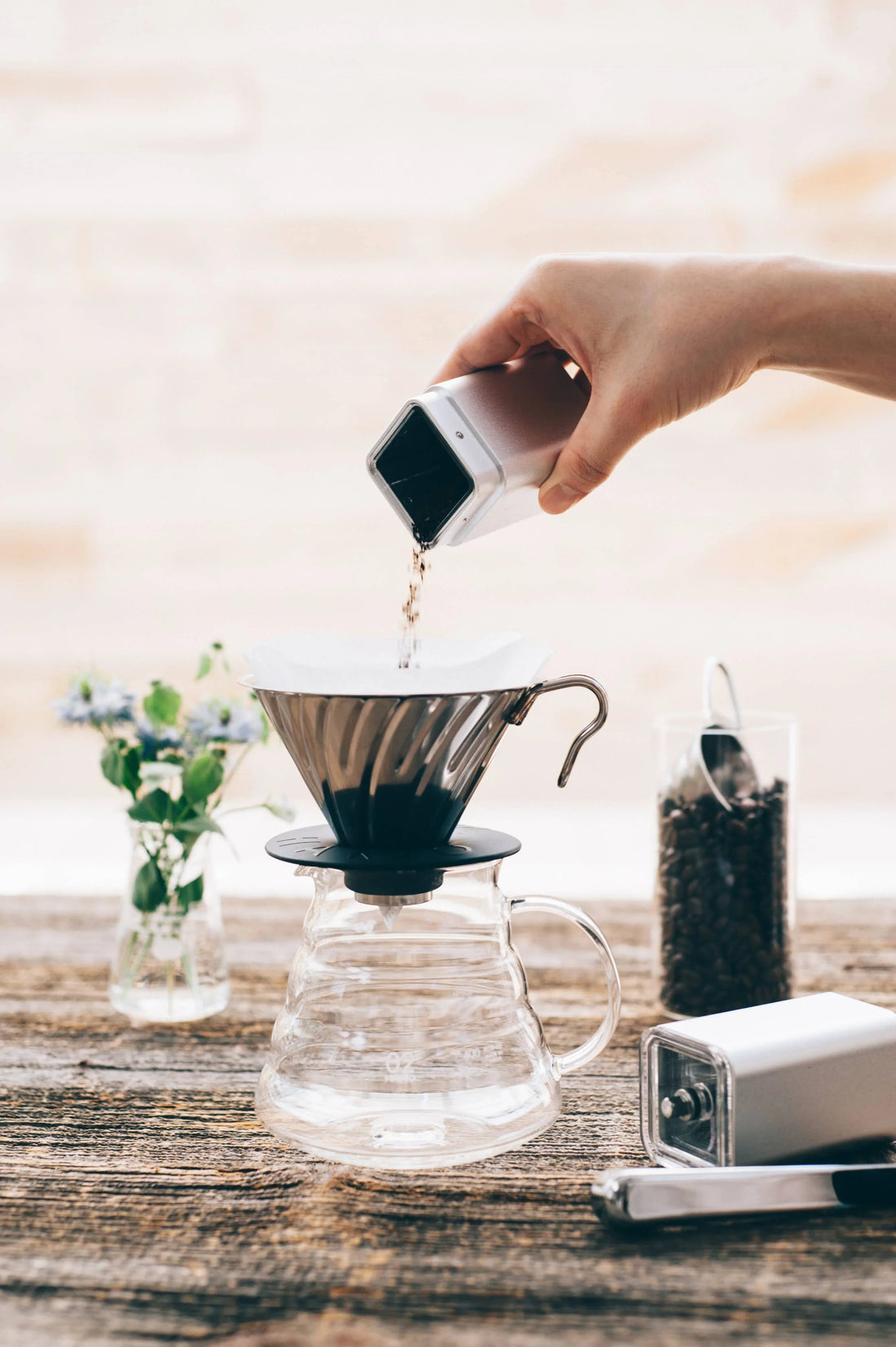 A pour-over coffee brewing setup at home with a dripper cone, paper filter, and glass carafe on a kitchen counter