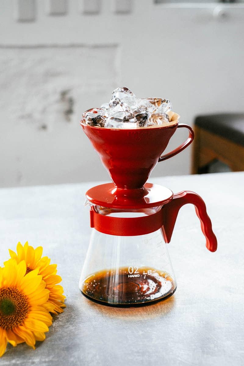 Hot coffee dripping through a pour-over dripper cone directly onto ice in a glass carafe, brewing Japanese-style iced coffee