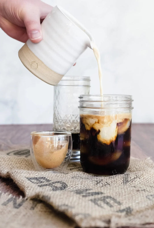 Hand pouring cream into iced coffee in mason jar on rustic burlap, Sound Coffee Bridgeport CT