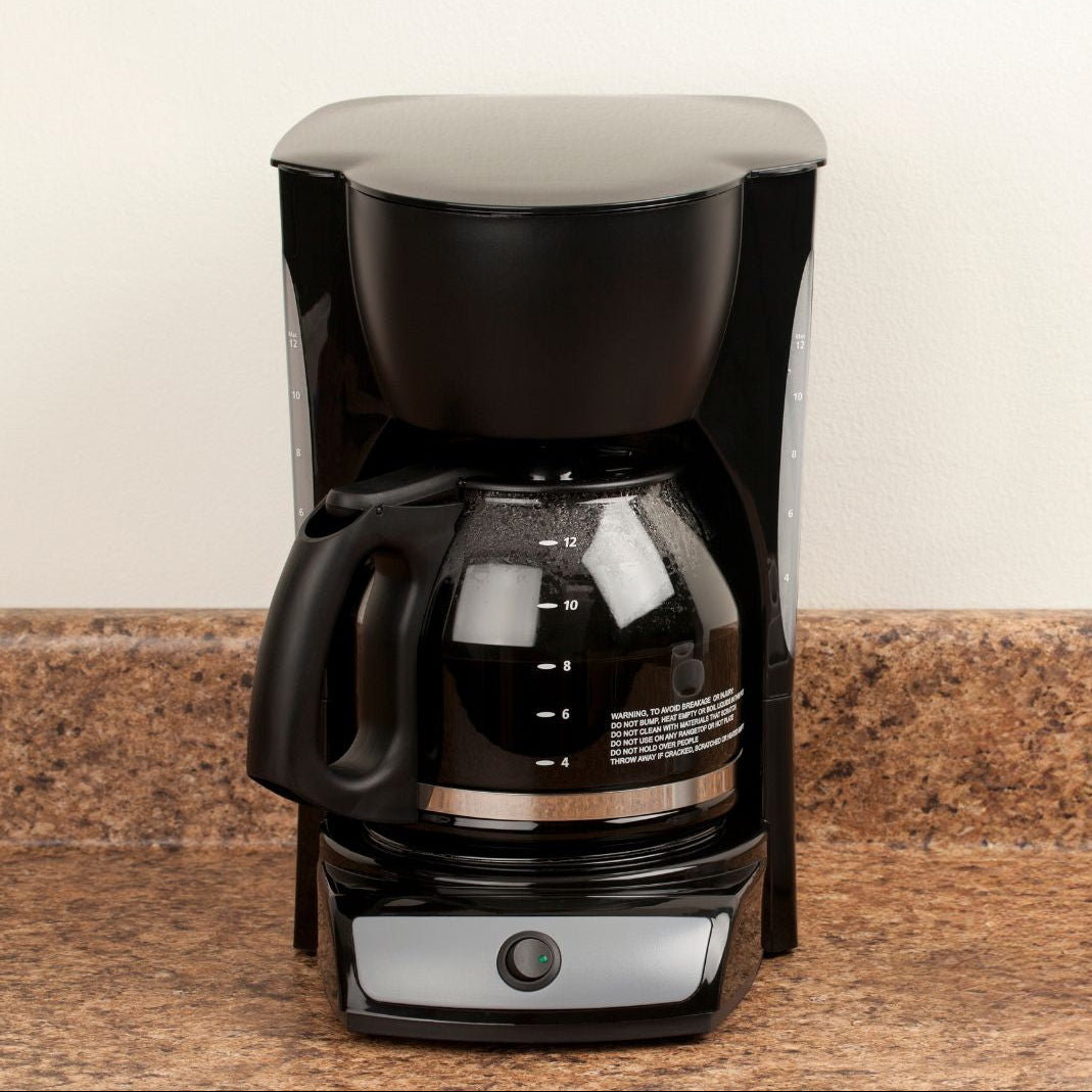 A black coffee maker with a glass carafe and clear lid, sitting on a speckled brown countertop against a light beige wall.