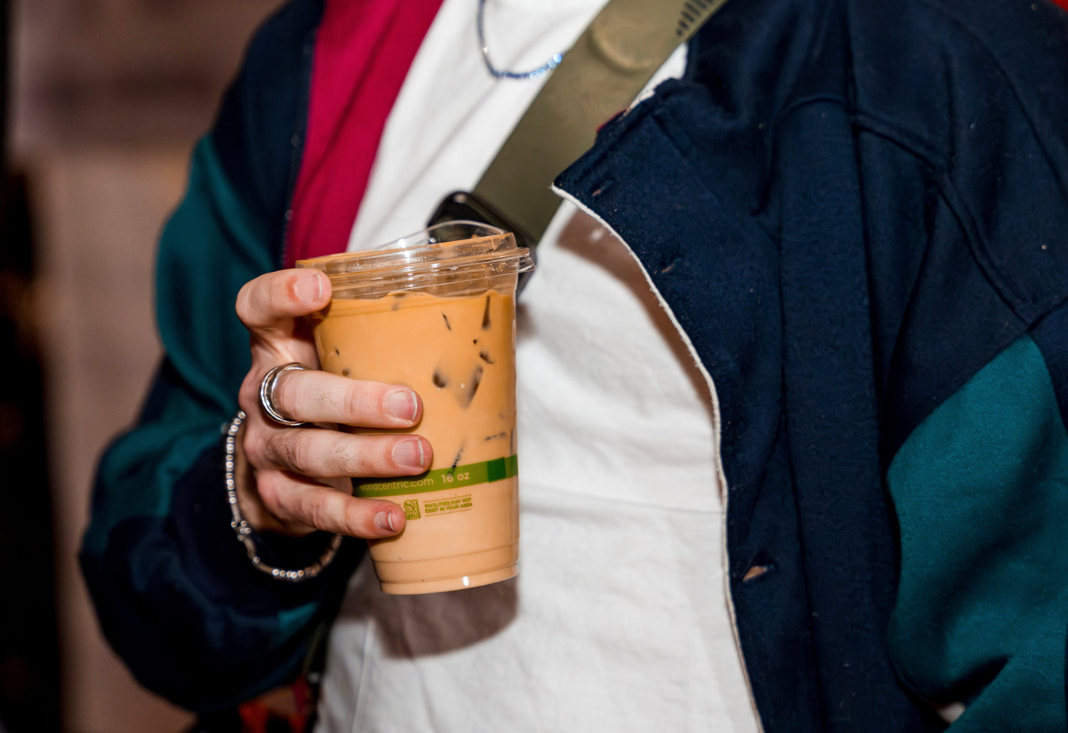 A closeup shot of an iced coffee for takeout holding by a man in a blue jacket