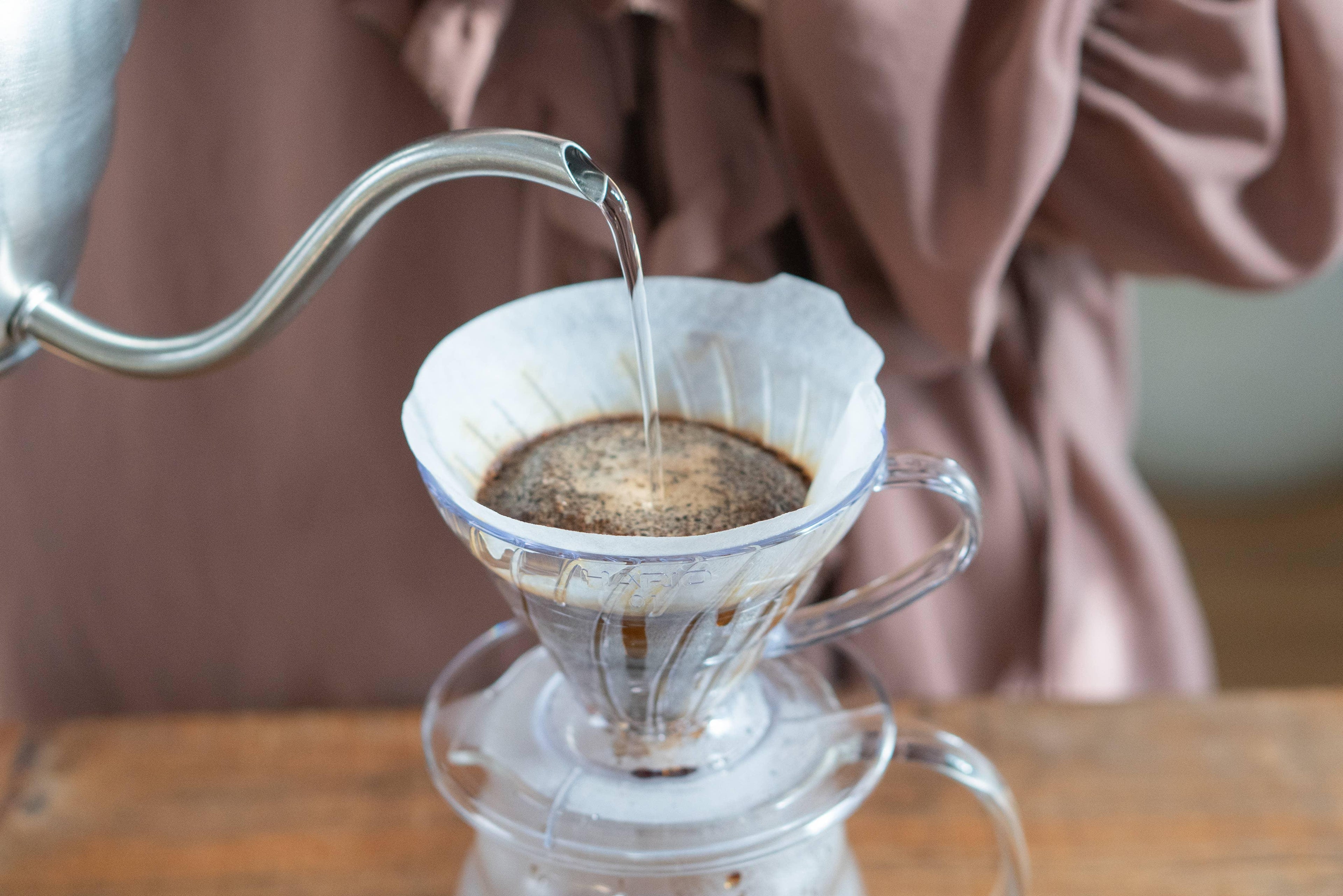 Pouring hot water over ground coffee in a glass pour over dripper at Sound Coffee